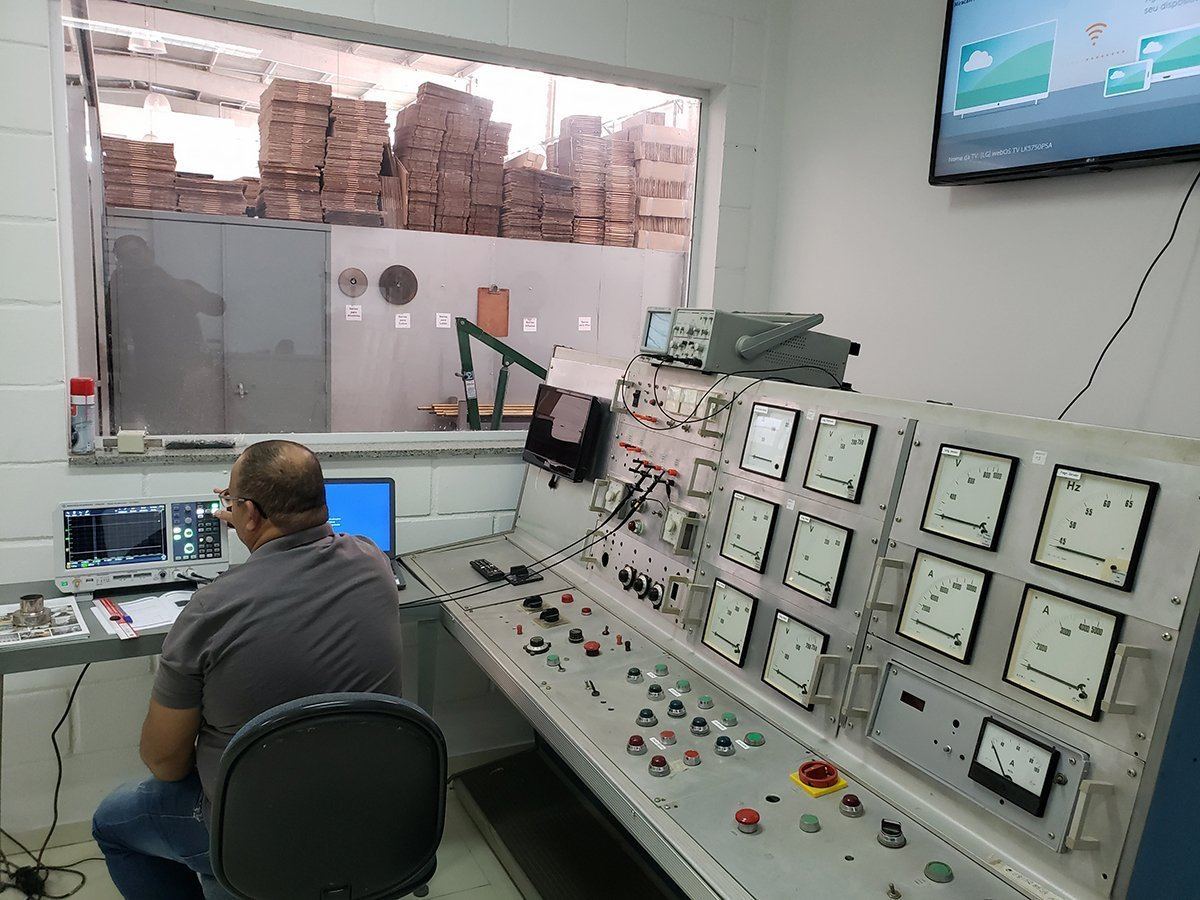 A technician at the factory laboratory control desk, facing a wall of analogue meters